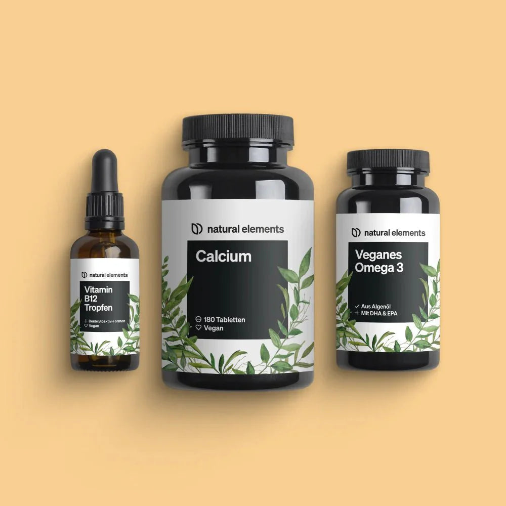 Drei Flaschen Nahrungsergänzungsmittel mit der Aufschrift „Vegan Hero Bundle“ von NATURAL ELEMENTS für Vitamin B12-Tropfen, Calcium-Tabletten und veganes Omega 3 auf beigem Hintergrund.